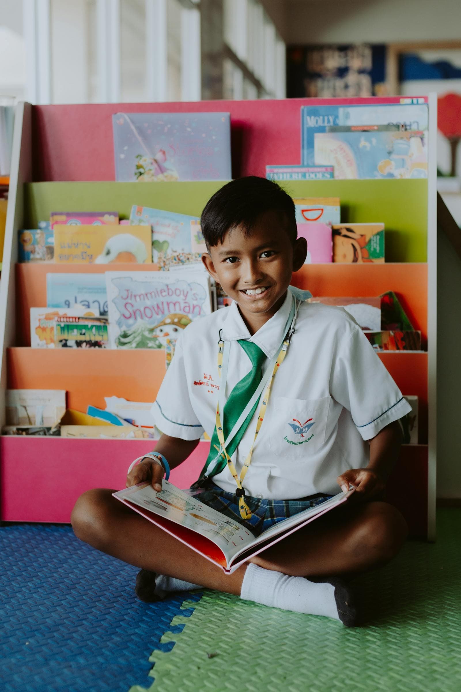 A student sits reading a picture book in front of a shelf of colorful library books